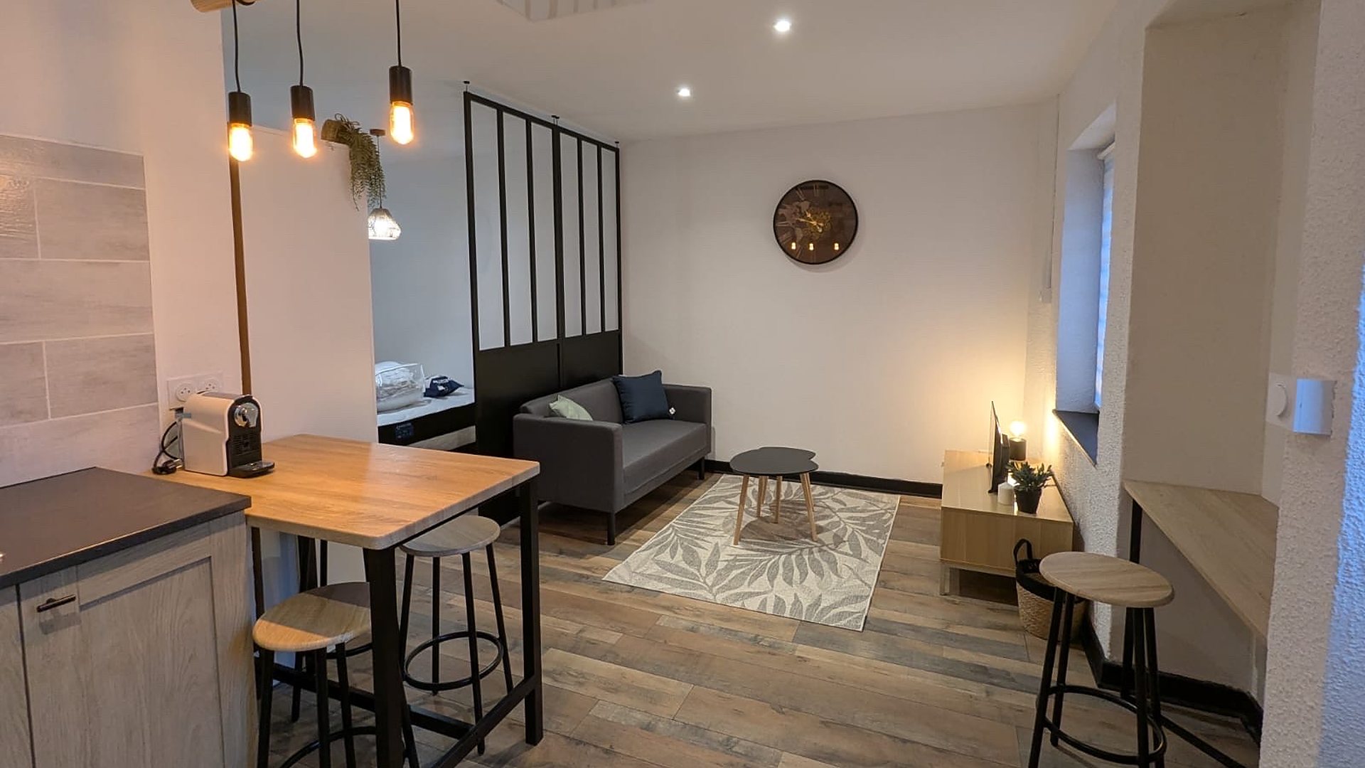 Appartement à Lyon : salon avec canapé gris, cuisine avec bar en bois, suspensions et verrière noire