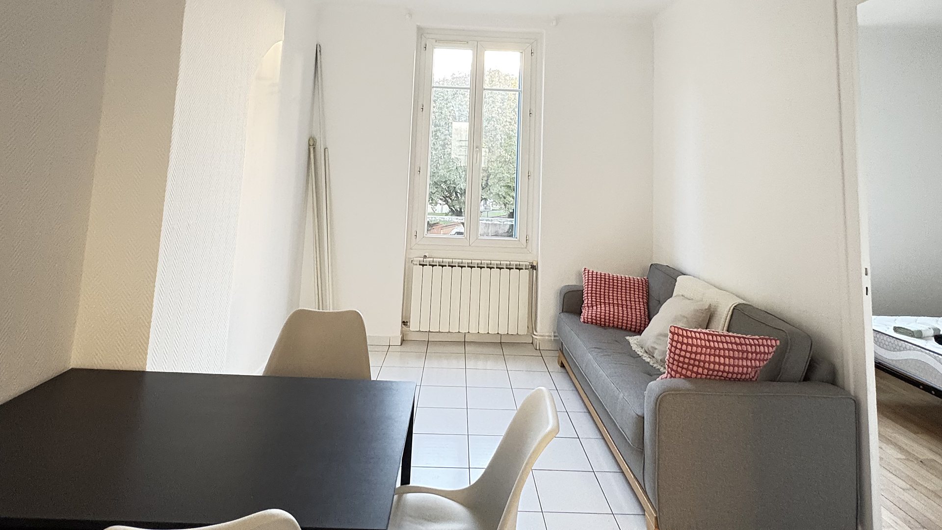 Séjour à Villeurbanne : canapé gris et coussins vichy rouges, table noire et chaises coque blanches